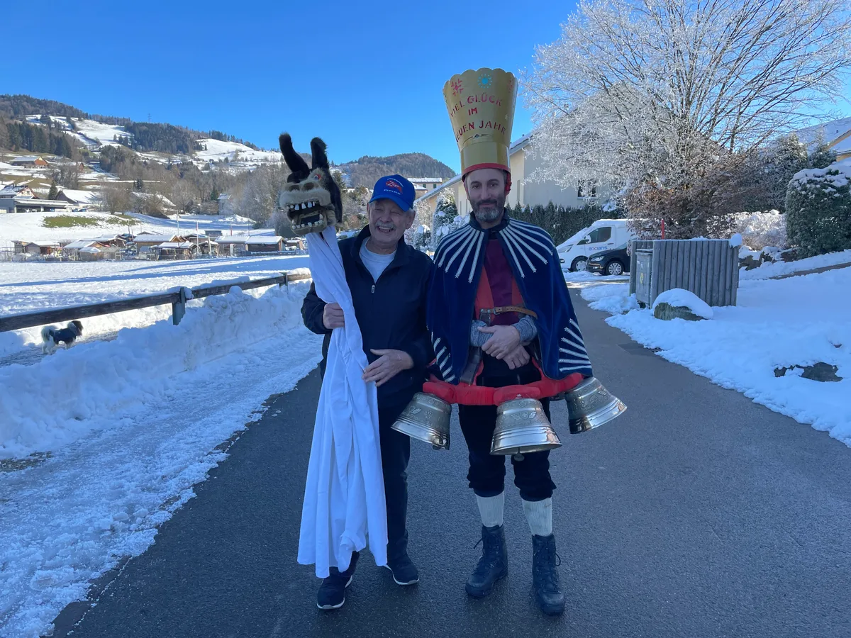 Ein Mann hält einen Schnappesel in der Hand, nebendran steht ein Silvesterchlaus. Es liegt Schnee.
